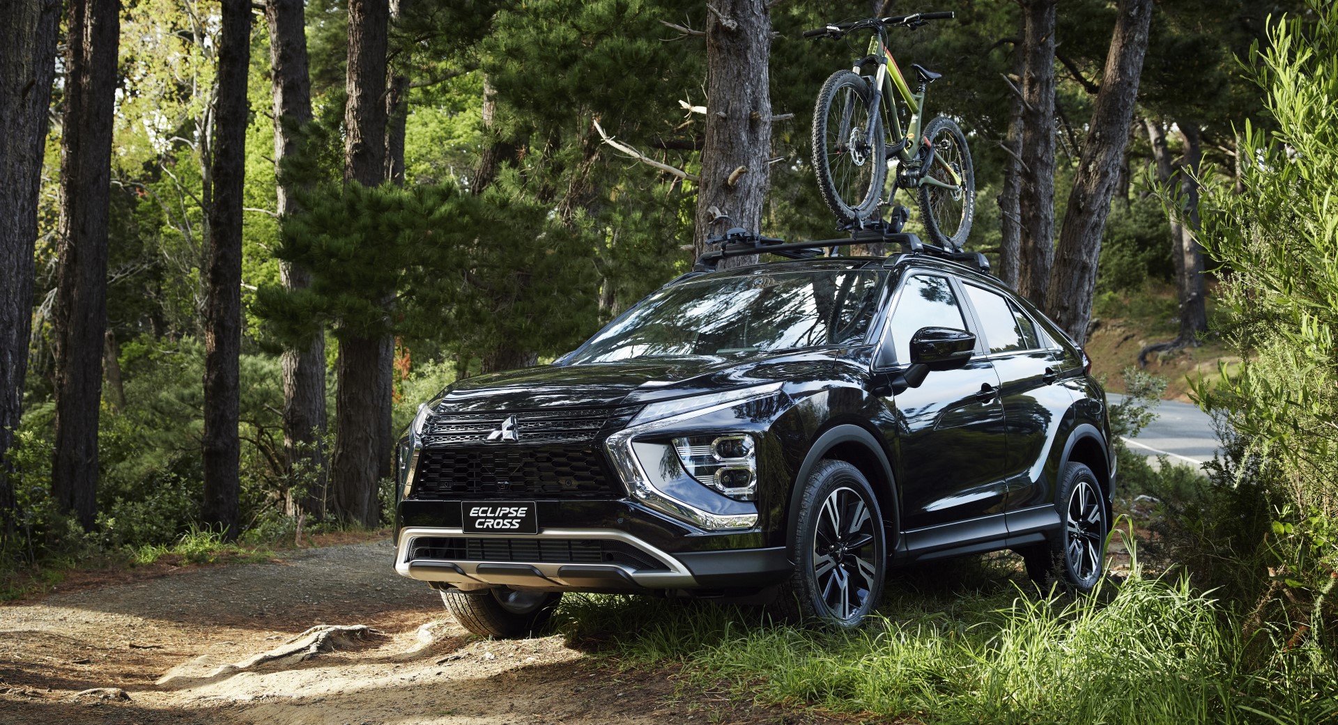 A black Mitsubishi Eclipse Cross with a mountain bike on top of its roof racks parked in a forest