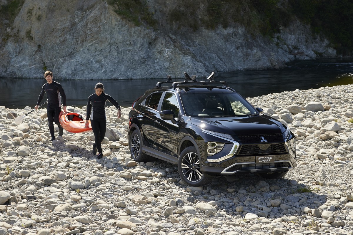 A Mitsubishi Eclipse Cross parked on a rocky river bank with two people carrying a kayak out of the water