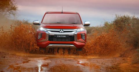 Front view of a red Triton driving through a puddle of mud with mud spraying either side